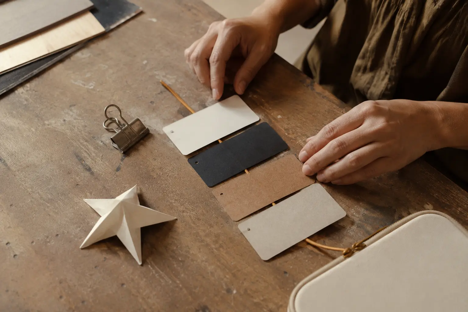 Fictional adult hands arranging blank material samples along a mustard cord on a working table